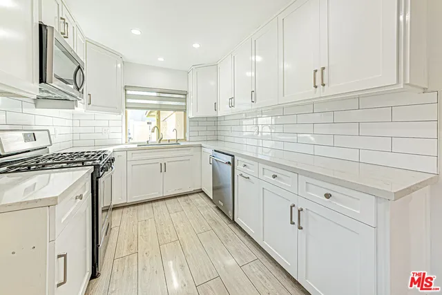 a kitchen with white cabinets appliances a sink and a window