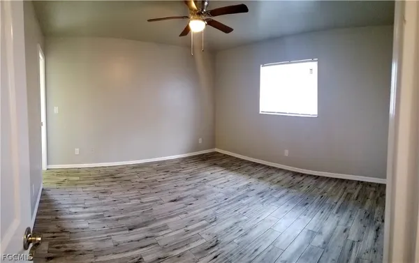 an empty room with wooden floor fan and windows