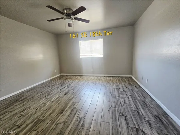 an empty room with wooden floor ceiling fan and windows