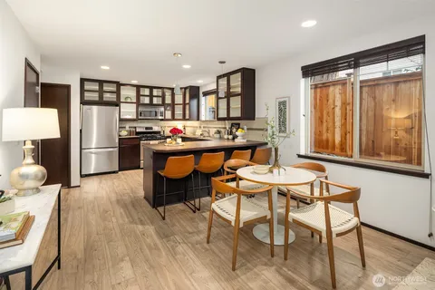 a room with stainless steel appliances kitchen island granite countertop a refrigerator a stove a sink dishwasher and a dining table with wooden cabinet
