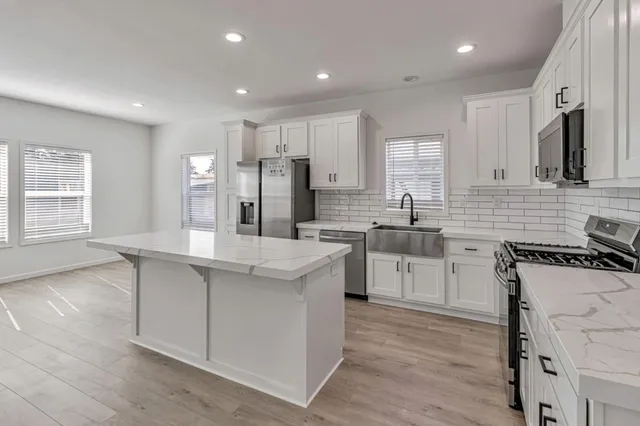 a kitchen with stainless steel appliances granite countertop a sink stove refrigerator and white cabinets with wooden floor