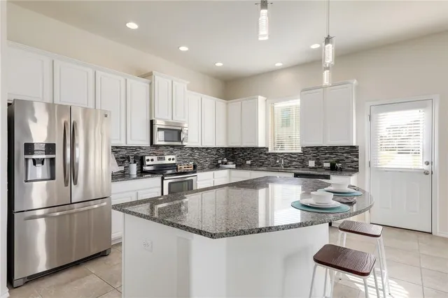 a kitchen with stainless steel appliances granite countertop a sink a stove a refrigerator cabinets and chairs