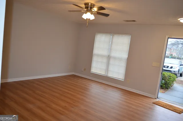 an empty room with wooden floor chandelier fan and windows