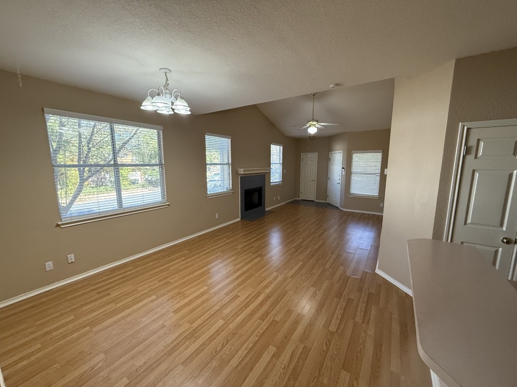 Unfurnished living room featuring vaulted ceiling, light wood-style flooring, a fireplace, a textured ceiling, and a chandelier