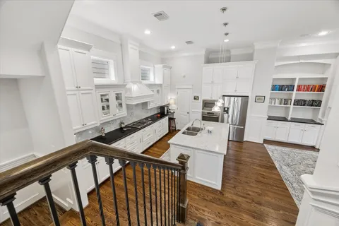 a open kitchen with stainless steel appliances kitchen island granite countertop a refrigerator a stove and white cabinets with wooden floor