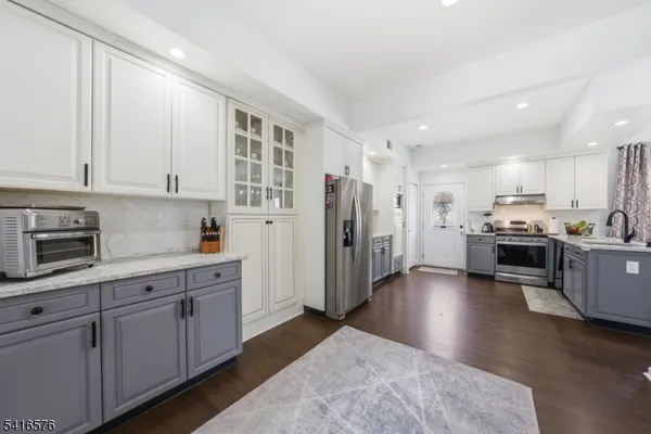 a kitchen with stainless steel appliances kitchen island granite countertop a refrigerator oven a sink dishwasher and white cabinets with wooden floor