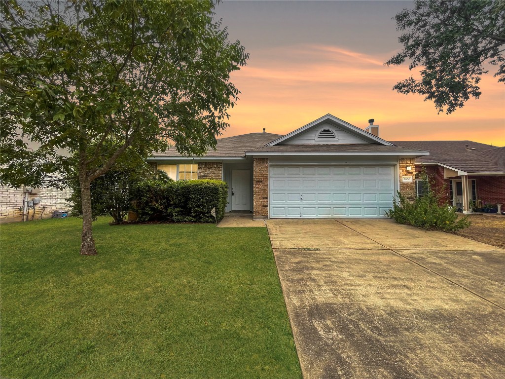 Single story home featuring brick siding, a yard, driveway, a chimney, and a garage