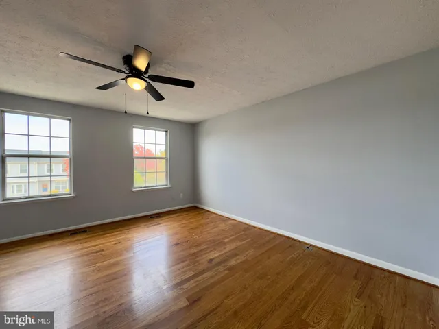 an empty room with wooden floor fan and windows