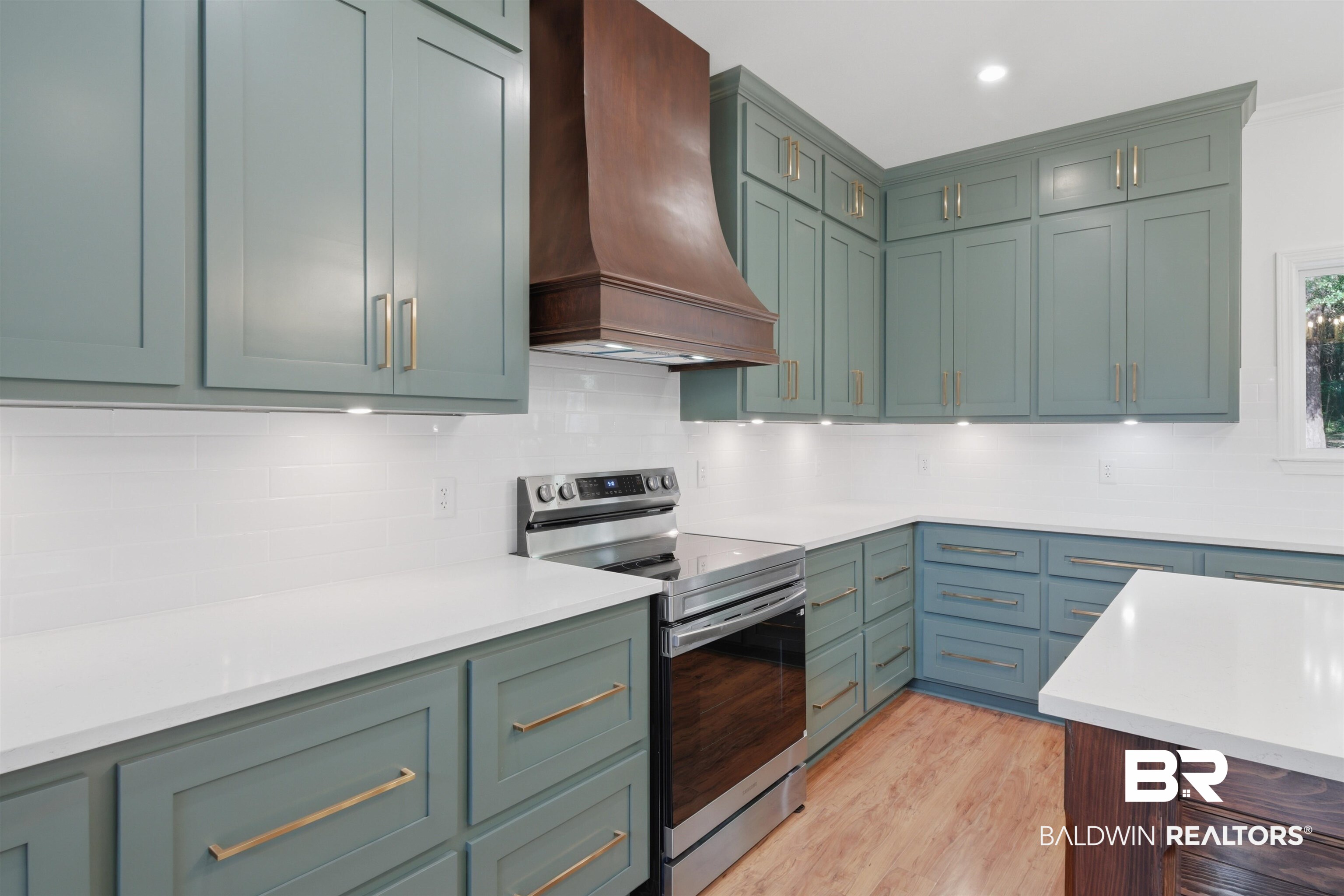 14128 Jackson Lane Foley, AL 36535 - Photo 11 of 36 Modern kitchen featuring light green cabinetry, white countertops, a wood-finish range hood, stainless steel appliances, and under-cabinet lighting