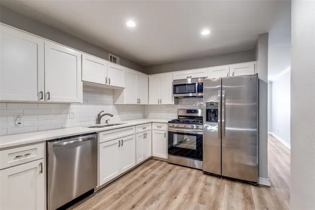 a kitchen with stainless steel appliances granite countertop a refrigerator a sink dishwasher a stove top oven a refrigerator with white cabinets and wooden floor