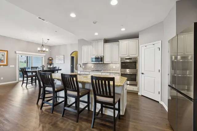 a kitchen with stainless steel appliances granite countertop a dining table chairs refrigerator and cabinets