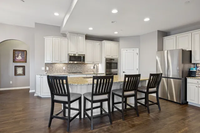 a kitchen with stainless steel appliances granite countertop a dining table chairs refrigerator and microwave