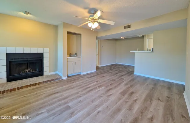 a view of an empty room with wooden floor a fireplace and a window