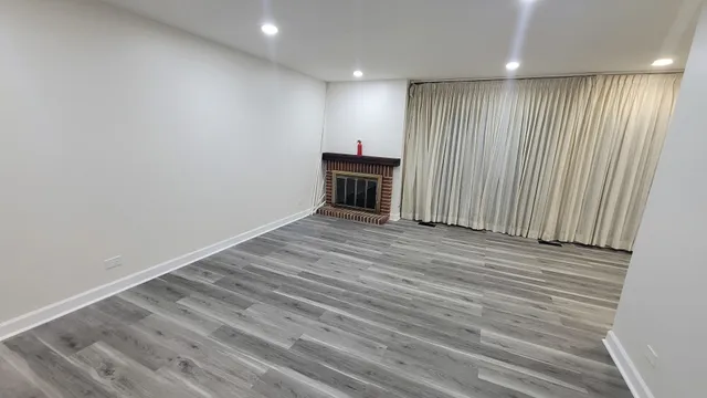 an empty room with wooden floor fireplace and windows