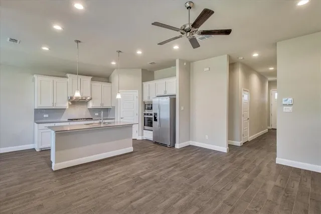 a large kitchen with a refrigerator a sink dishwasher a stove and white cabinets with wooden floor