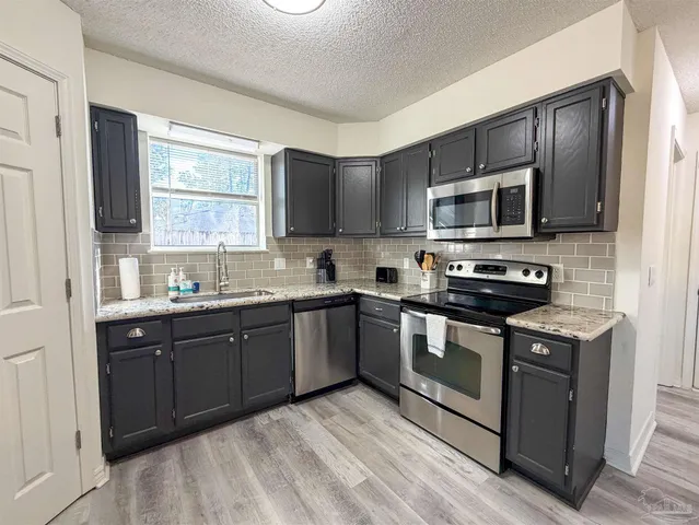 a kitchen with stainless steel appliances granite countertop a stove top oven a sink dishwasher a microwave oven and a refrigerator with wooden floor