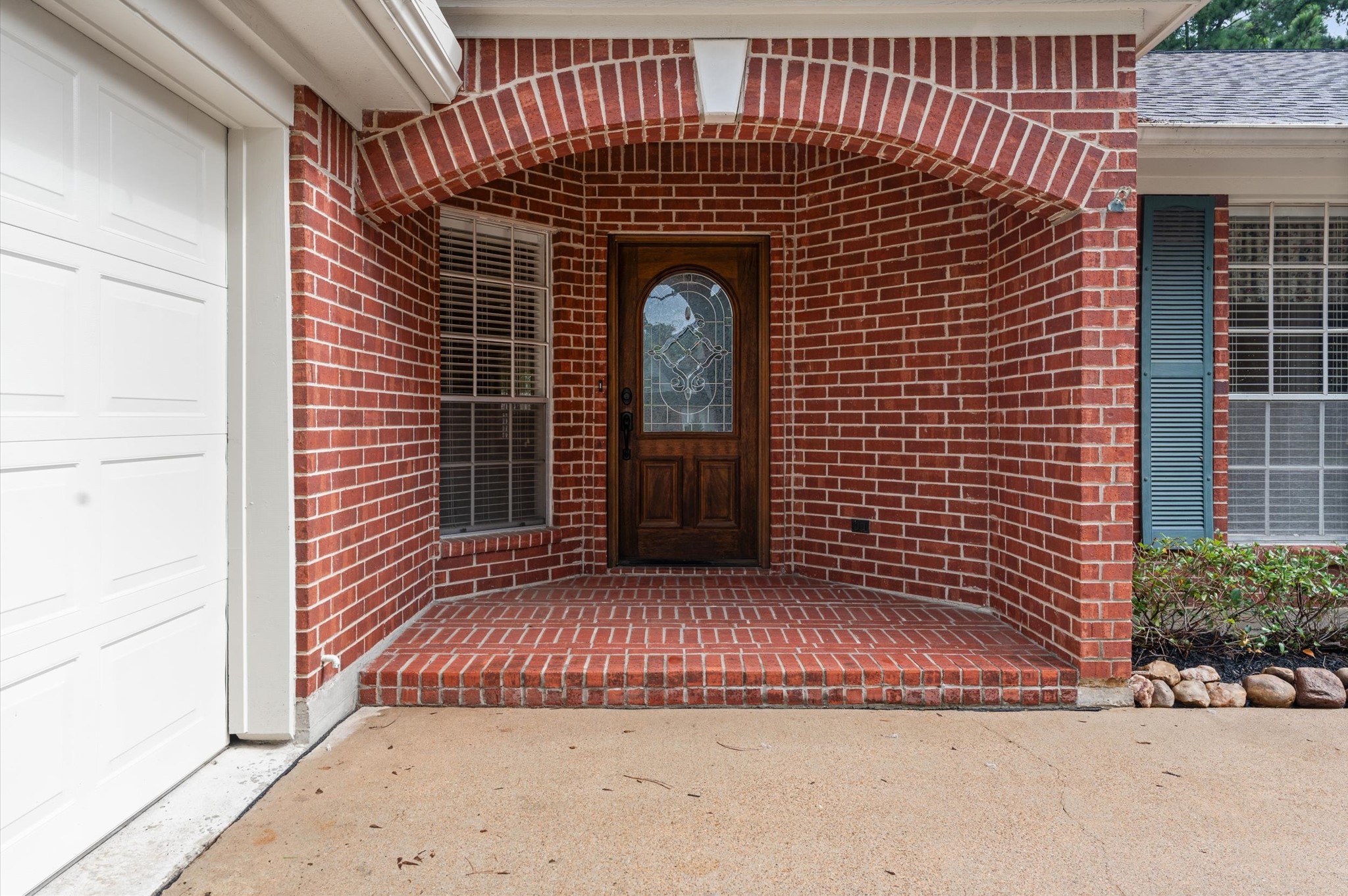 17618 Mill Springs Drive Spring, TX 77379 - Photo 3 of 26 Charming brick entryway with a wooden front door featuring decorative glass. The entrance is framed by large windows and a covered porch, offering a welcoming and classic look.
