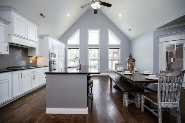 a kitchen with stainless steel appliances granite countertop a stove a refrigerator a sink a dining table and chairs with wooden floor