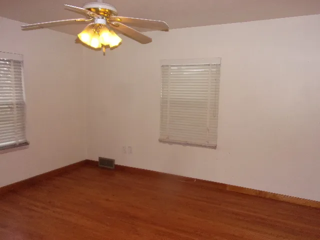 an empty room with a wooden floor and chandelier fan