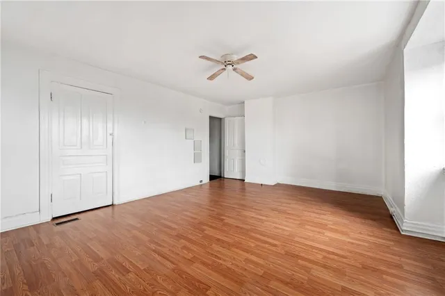 an empty room with wooden floor ceiling fan and windows