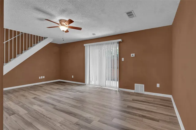 a view of an empty room with wooden floor and fan