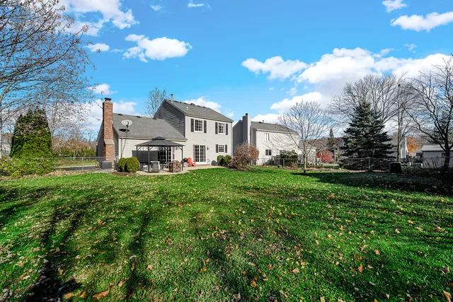 a view of a white house with a big yard plants and large trees