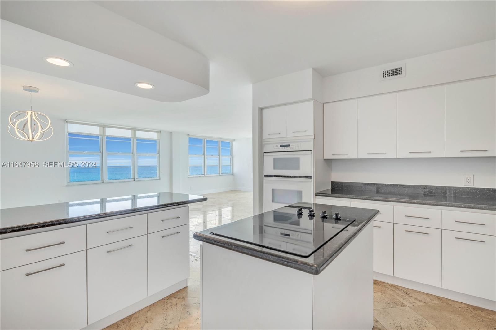 5151 Collins Avenue, Unit 1627 Miami Beach, FL 33140 - Photo 11 of 28 a kitchen with kitchen island granite countertop a sink white cabinets and white appliances