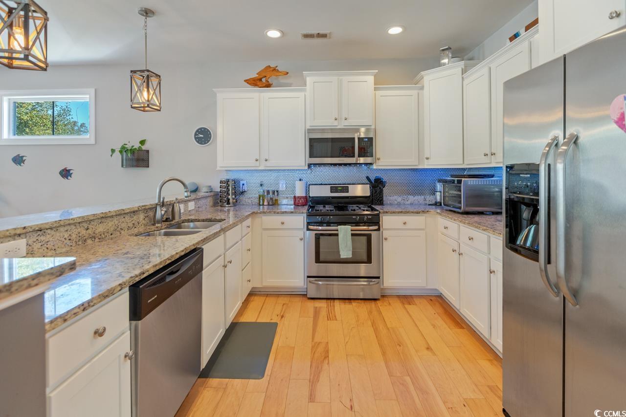 3887 Spanner Way Murrells Inlet, SC 29576 - Photo 11 of 32 Kitchen featuring appliances with stainless steel finishes, white cabinetry, tasteful backsplash, light stone countertops, and pendant lighting