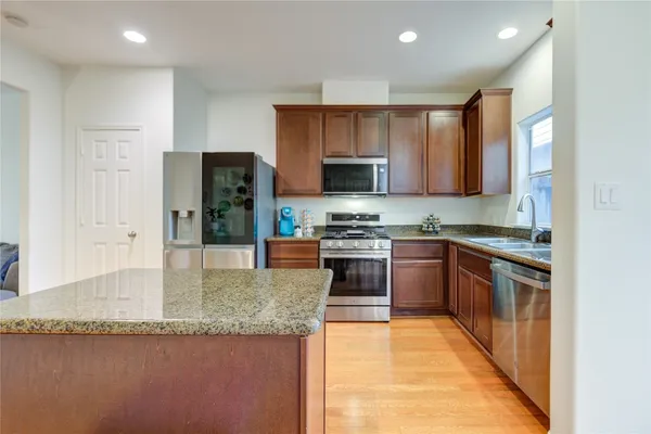 a kitchen with stainless steel appliances granite countertop a refrigerator a stove and a sink with wooden cabinets
