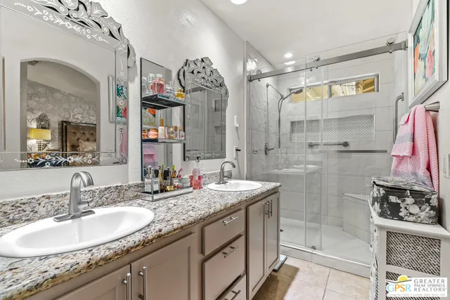 a bathroom with a granite countertop double vanity sink mirror and shower
