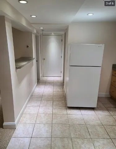 a view of a refrigerator in kitchen and an empty room in wooden floor