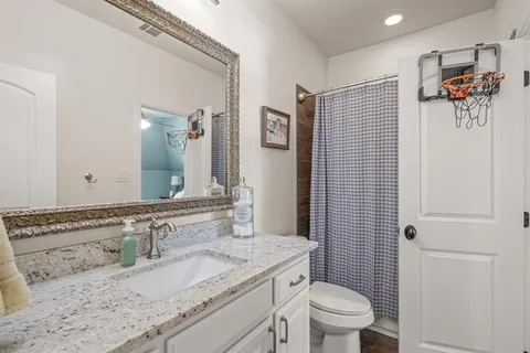 a bathroom with a granite countertop sink a toilet a mirror and shower curtain
