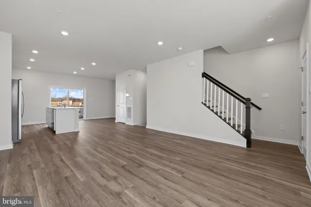 a view of an empty room with wooden floor kitchen view and a window