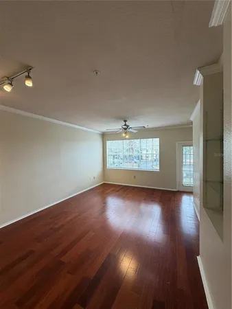 a view of an empty room with wooden floor and a ceiling fan