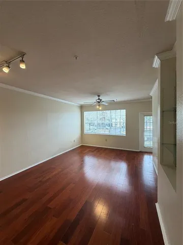 a view of an empty room with wooden floor and a ceiling fan