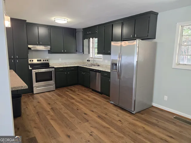 a kitchen with stainless steel appliances granite countertop a refrigerator a stove a sink and dishwasher with wooden floor