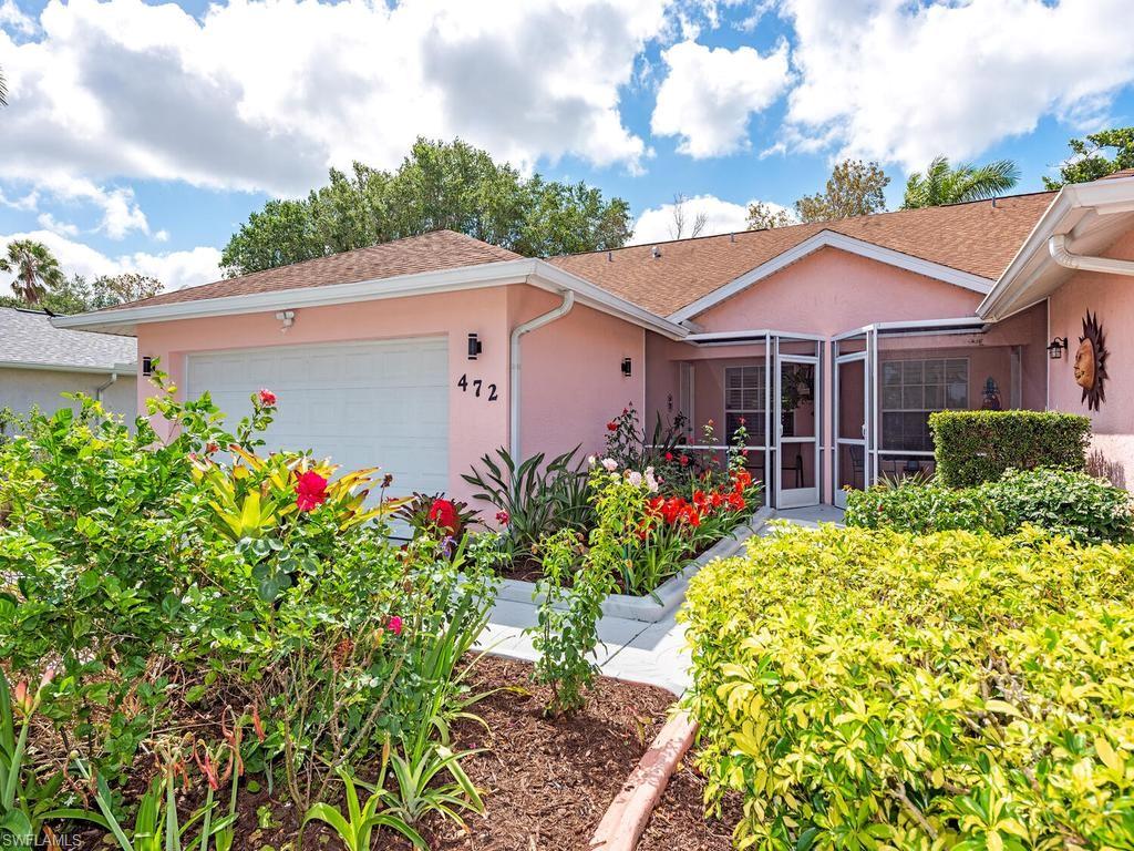 472 St Andrews Boulevard Naples, FL 34113 - Photo 7 of 18 a view of a white house with a flower garden plants and large tree