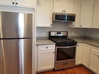 a kitchen with stainless steel appliances granite countertop white cabinets and wooden floor