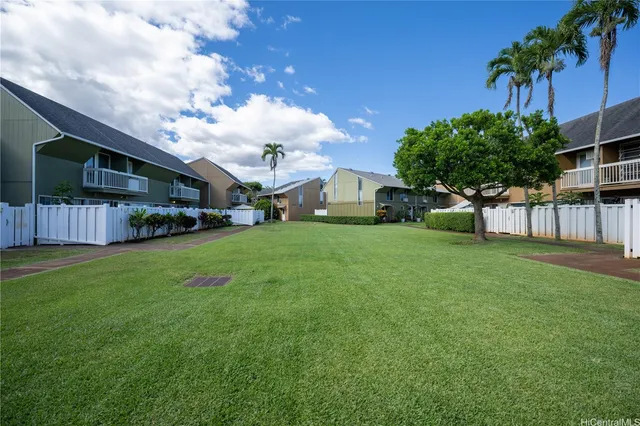 a view of a white house in front of a big yard with potted plants and large trees