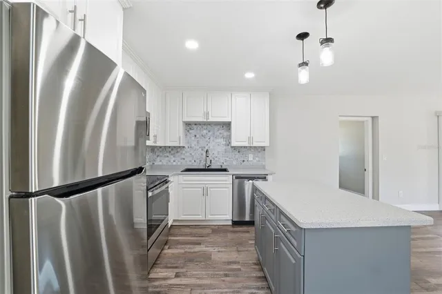 a kitchen with stainless steel appliances granite countertop a refrigerator a sink and white cabinets