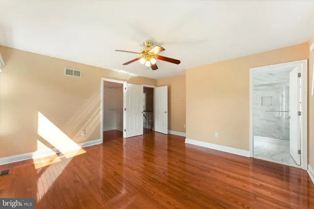 a view of an empty room with wooden floor and a ceiling fan
