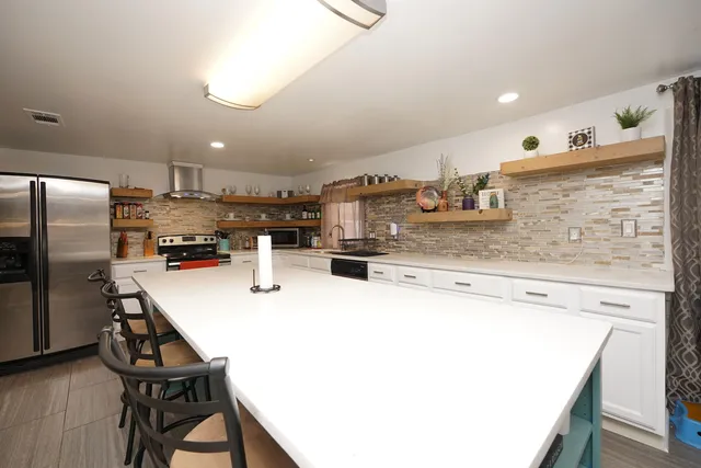 a kitchen with stainless steel appliances kitchen island granite countertop a refrigerator a stove and a sink with cabinets