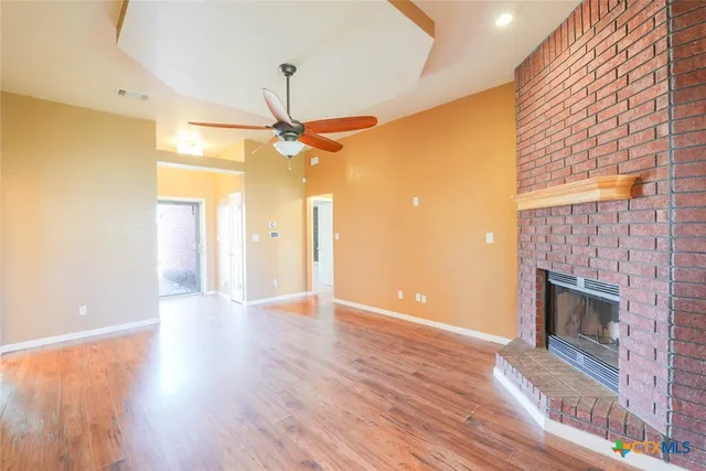 a view of an empty room with wooden floor and a fireplace