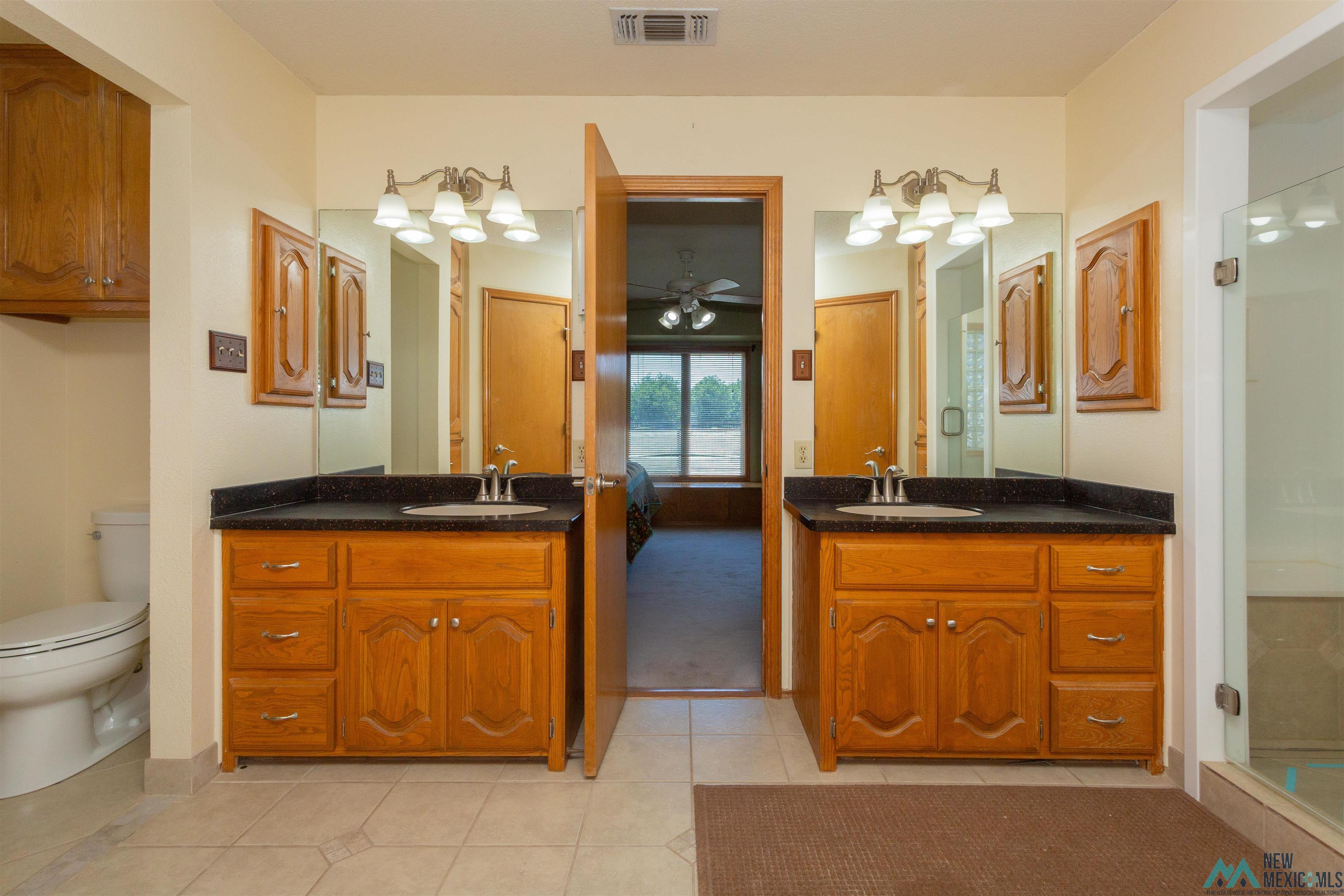 2012 South Haldeman Road Artesia, NM 88210 - Photo 51 of 96 Dual vanity with wood-finish cabinetry, dark countertops, and ample mirror space
