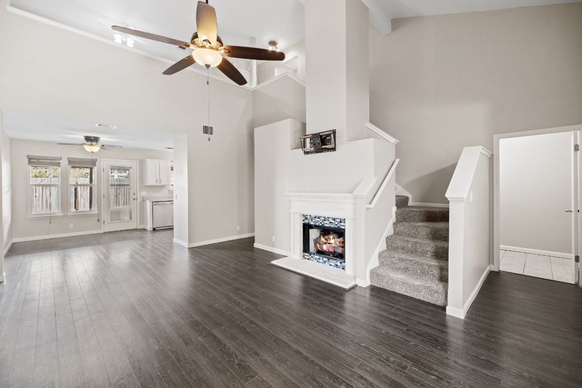413 Clarks Way Hutto, TX 78634 - Photo 2 of 34 Living room featuring a high ceiling, a lit fireplace, a ceiling fan, dark wood-type flooring, and stairway
