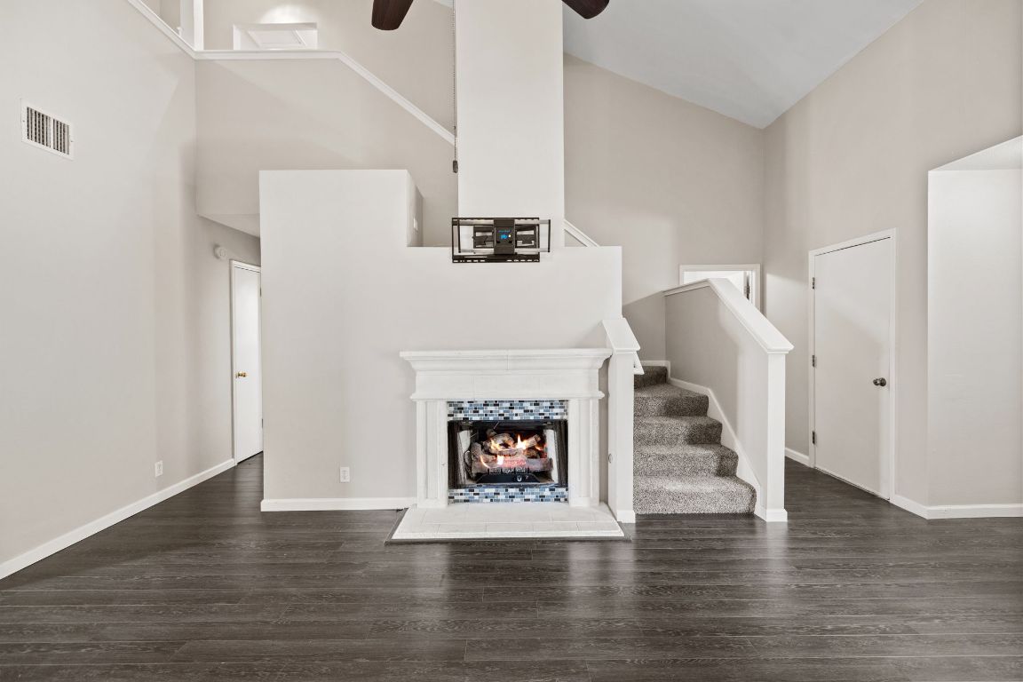 413 Clarks Way Hutto, TX 78634 - Photo 4 of 34 Unfurnished living room featuring a towering ceiling, dark wood-style flooring, stairs, a ceiling fan, and a warm lit fireplace
