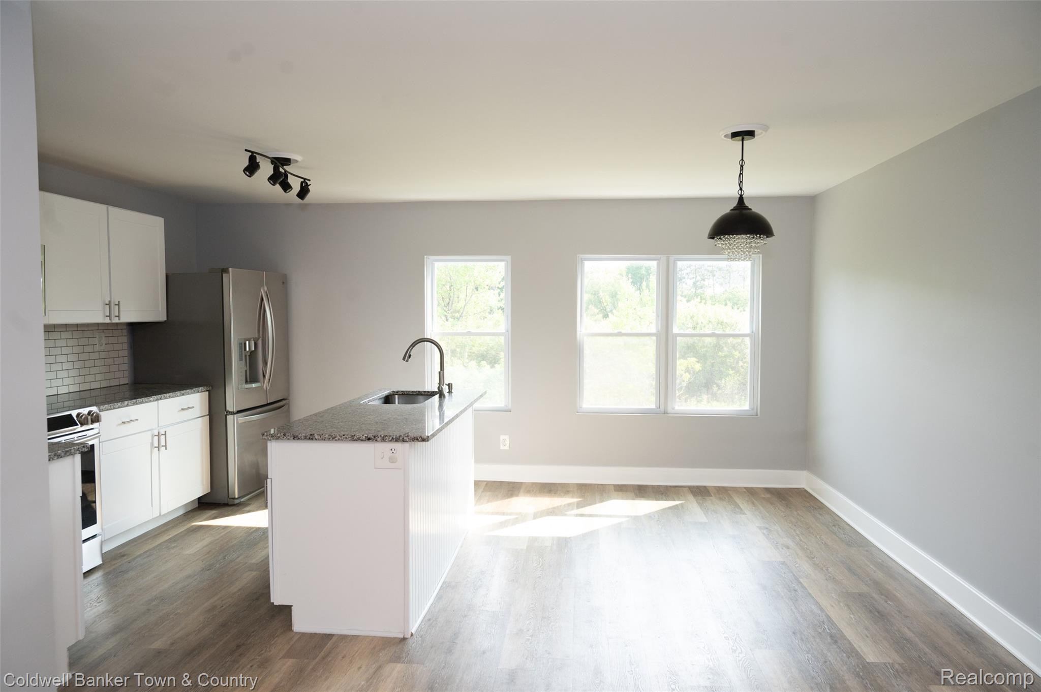 5080 Chilson Road Howell, MI 48843 - Photo 6 of 16 Open-concept kitchen and dining area featuring a central island with sink, white shaker cabinetry, stainless steel appliances, and wood-finish flooring