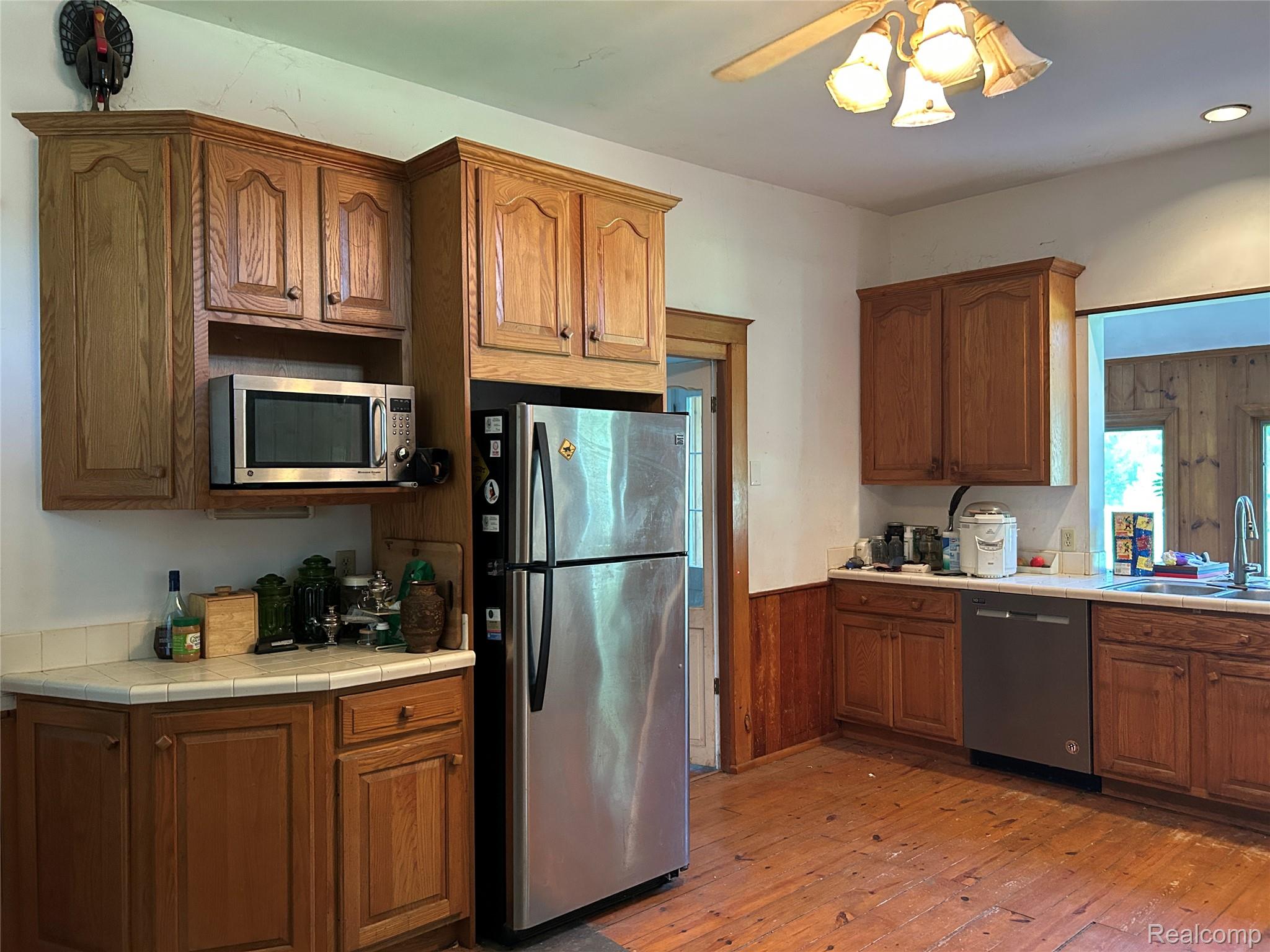 1285 Grange Hall Road Fenton, MI 48430 - Photo 12 of 50 Kitchen featuring wood-finish flooring, wood cabinetry, built-in microwave, stainless steel refrigerator, and a ceiling fan with integrated lighting