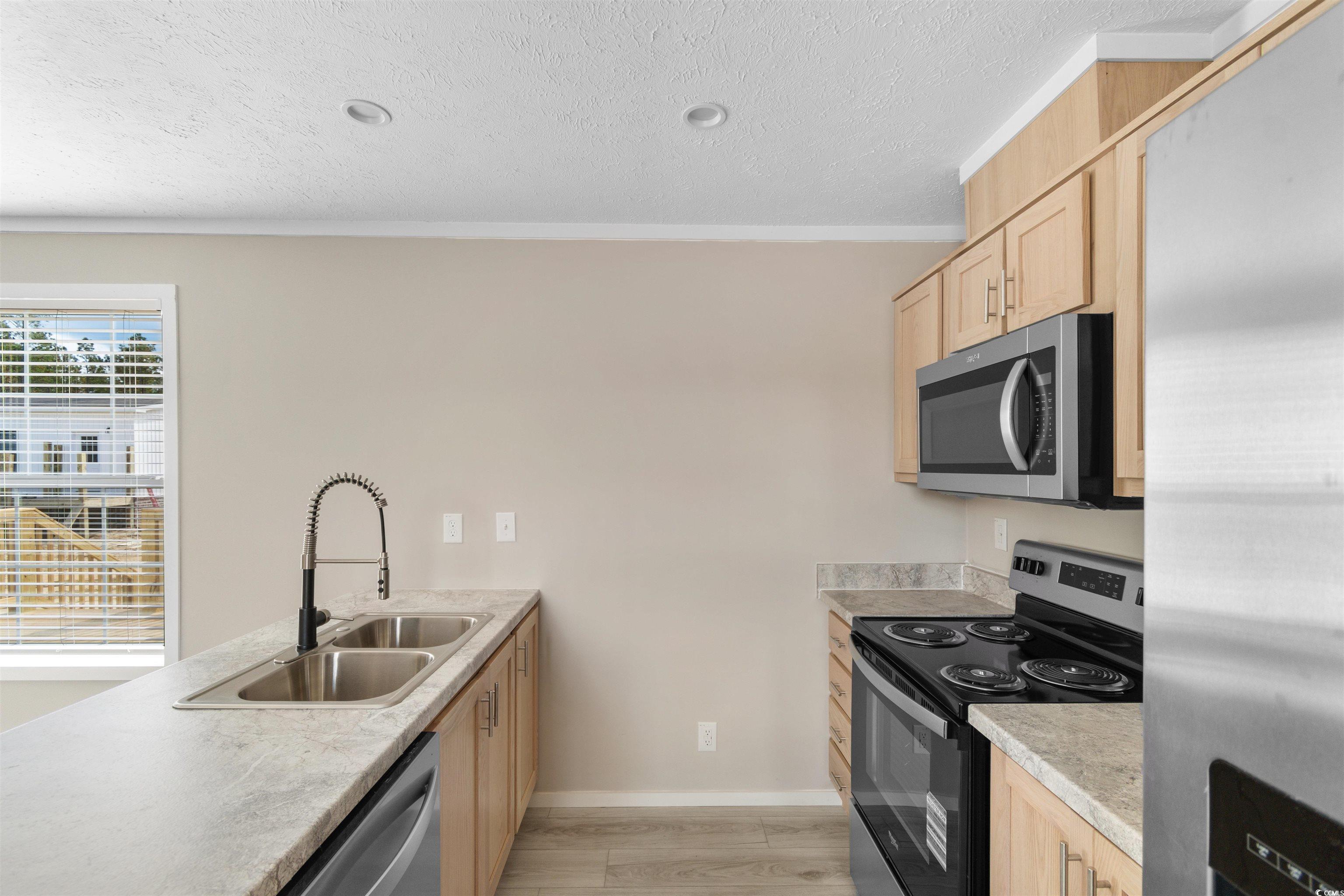 121 Feather Drive Georgetown, SC 29440 - Photo 12 of 40 Kitchen with light brown cabinets, appliances with stainless steel finishes, light countertops, light wood-type flooring, and a textured ceiling