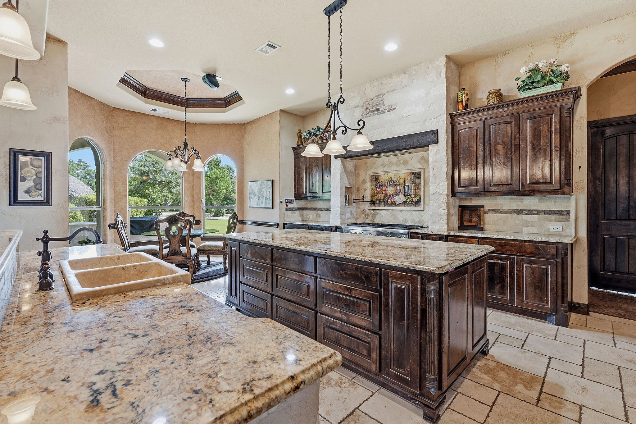 816 Brave Face Street Leander, TX 78641 - Photo 6 of 40 A spacious kitchen with rich wood cabinetry, stone countertops, and arched windows offering garden views.